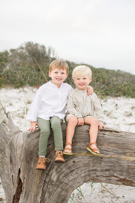 brothers sit on a log at the beach while a 30a photographer takes a picture